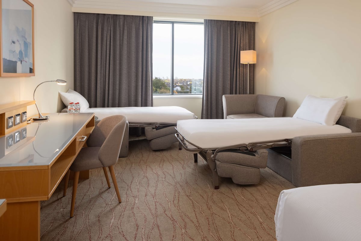 Une chambre d’hôtel avec deux lits, un bureau, une chaise et une fenêtre avec des rideaux.