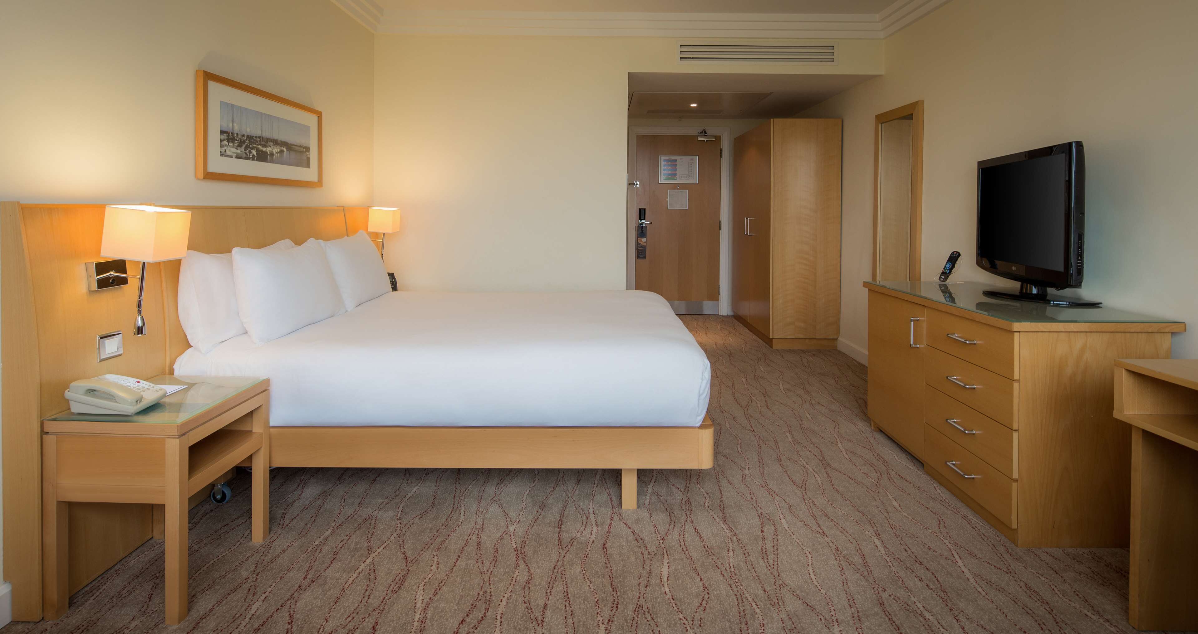 Habitación de hotel con una cama grande, un escritorio con teléfono, televisión y armario.