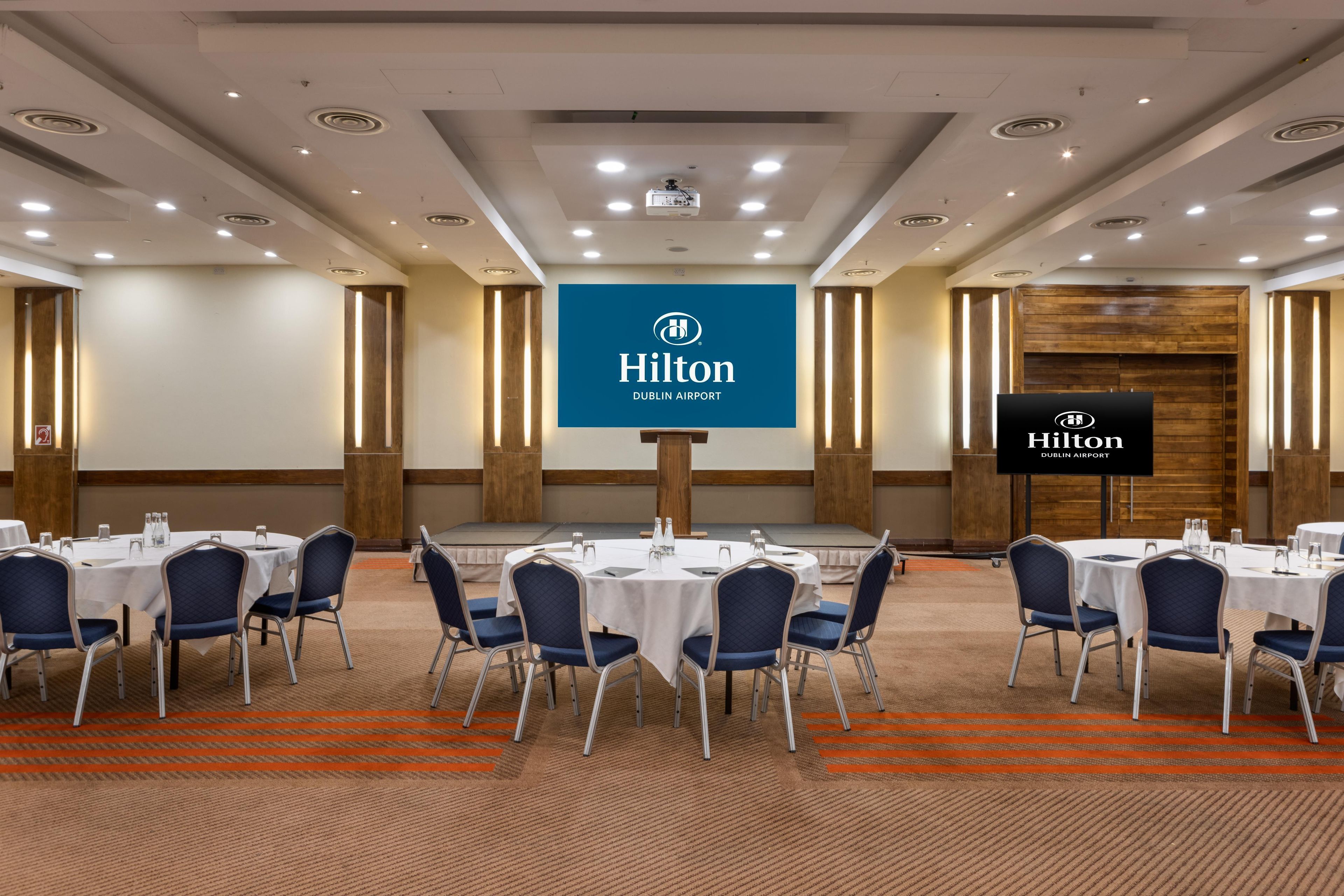 A conference room with round tables, blue chairs, and a stage.