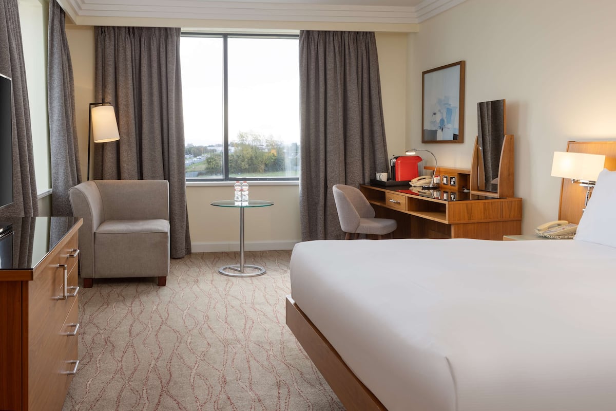 Une chambre d’hôtel avec un lit, un bureau, une chaise, une petite table et une fenêtre avec des rideaux.