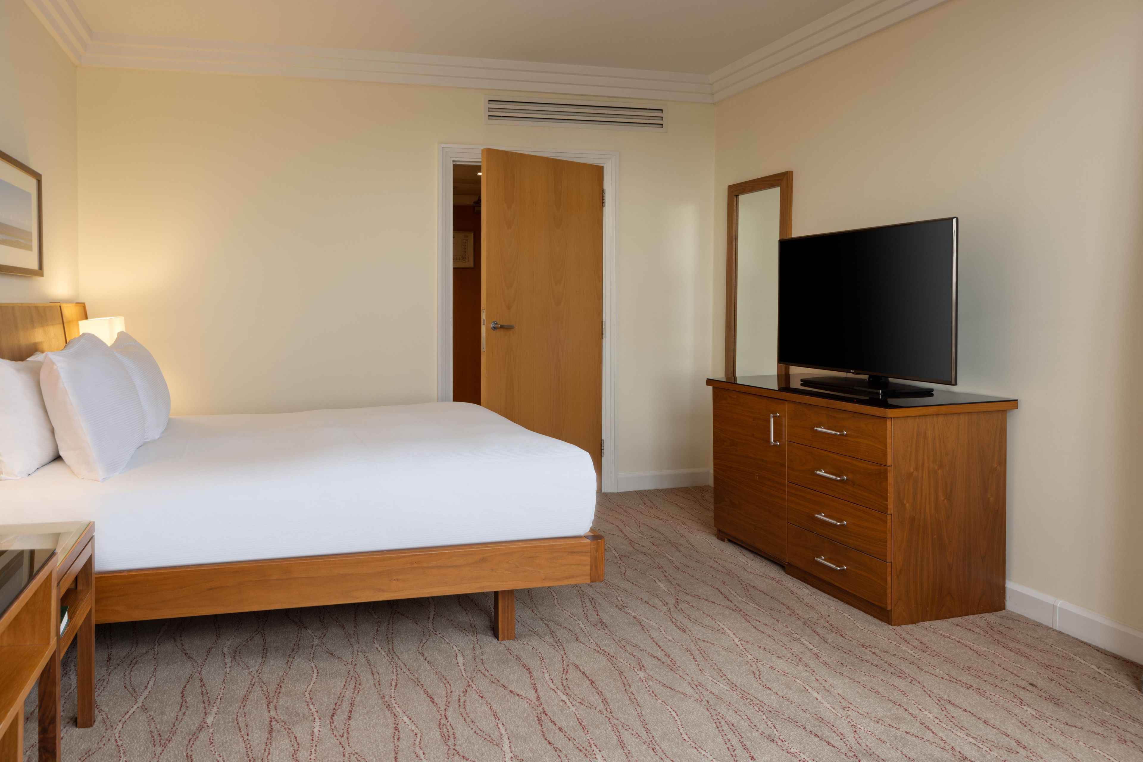 A hotel room with a bed, a television on a wooden cabinet, and a door leading to another room.