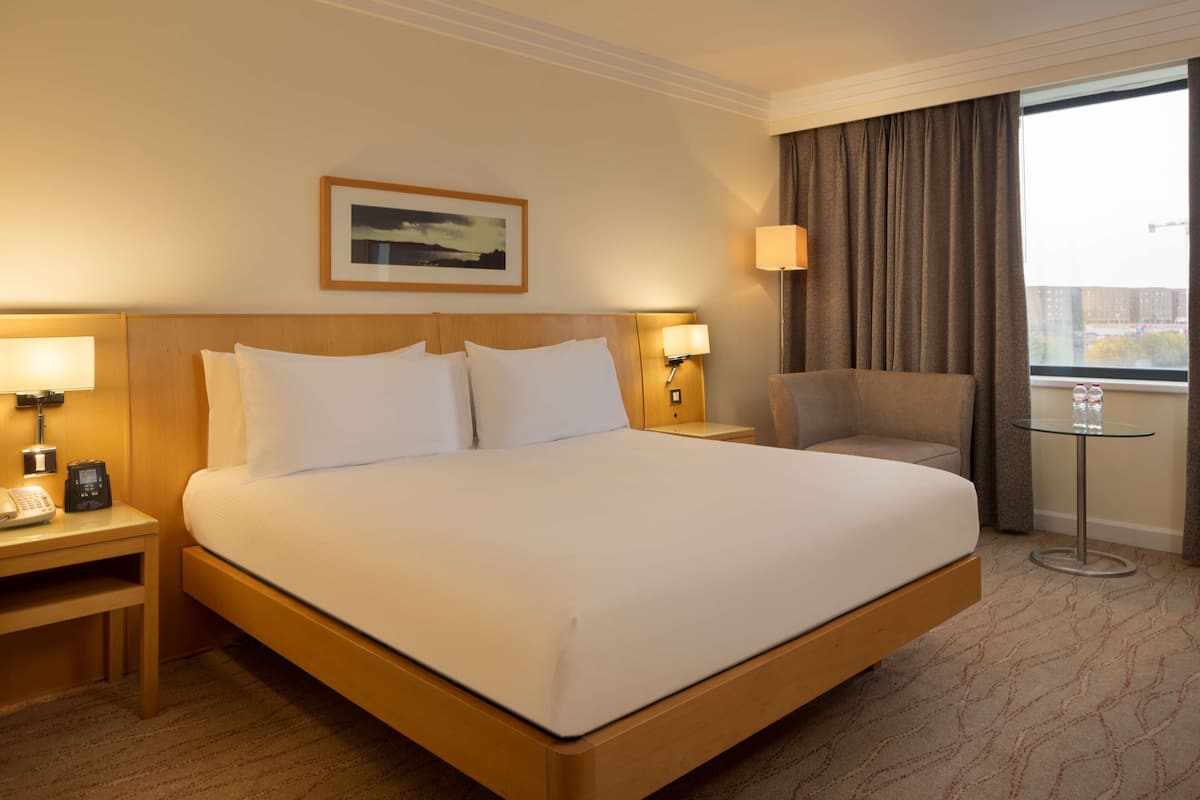 Une chambre d’hôtel avec un grand lit, des lampes de chevet, une chaise, une petite table et une fenêtre avec des rideaux.