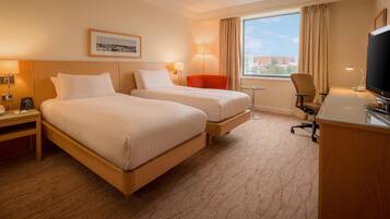 A hotel room with two beds, a desk, a chair, a TV, and a window with a view.