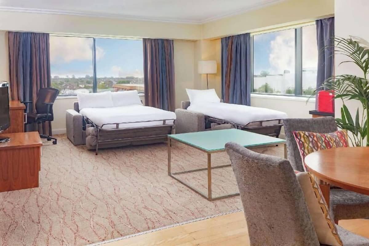 Une chambre d’hôtel avec deux lits, un bureau, une chaise, une table et une vue sur la ville.