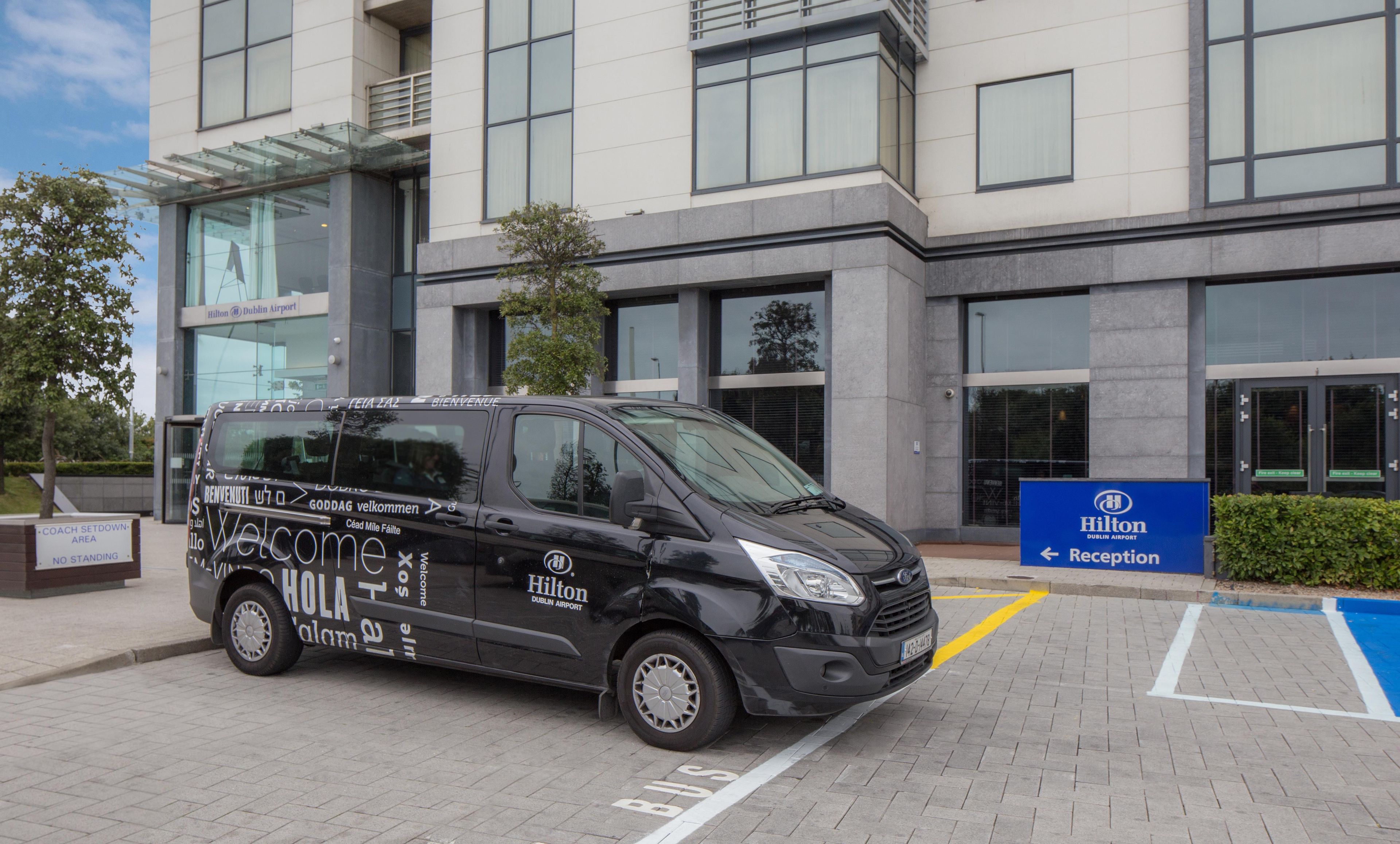 Een zwarte bestelwagen geparkeerd voor een gebouw met een bord waarop 'Hilton Dublin Airport Reception' staat.