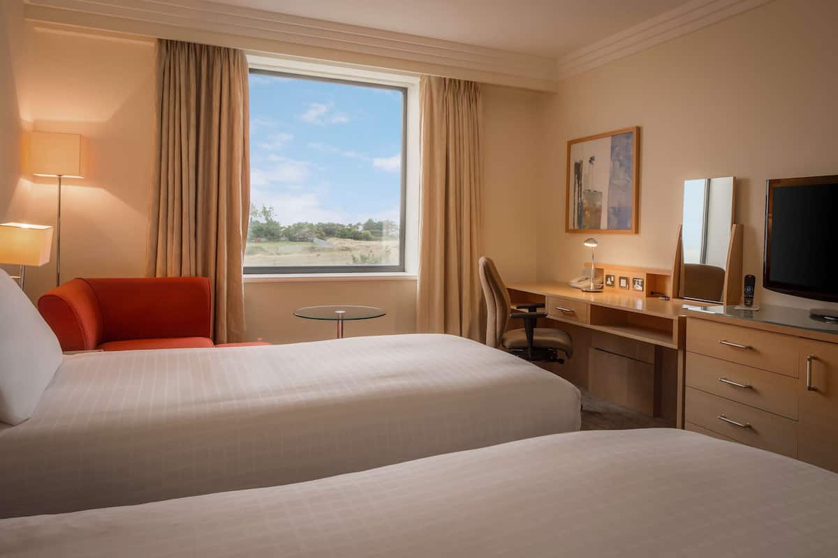 Une chambre d’hôtel avec deux lits, un bureau, une chaise, une télévision et une fenêtre avec des rideaux.