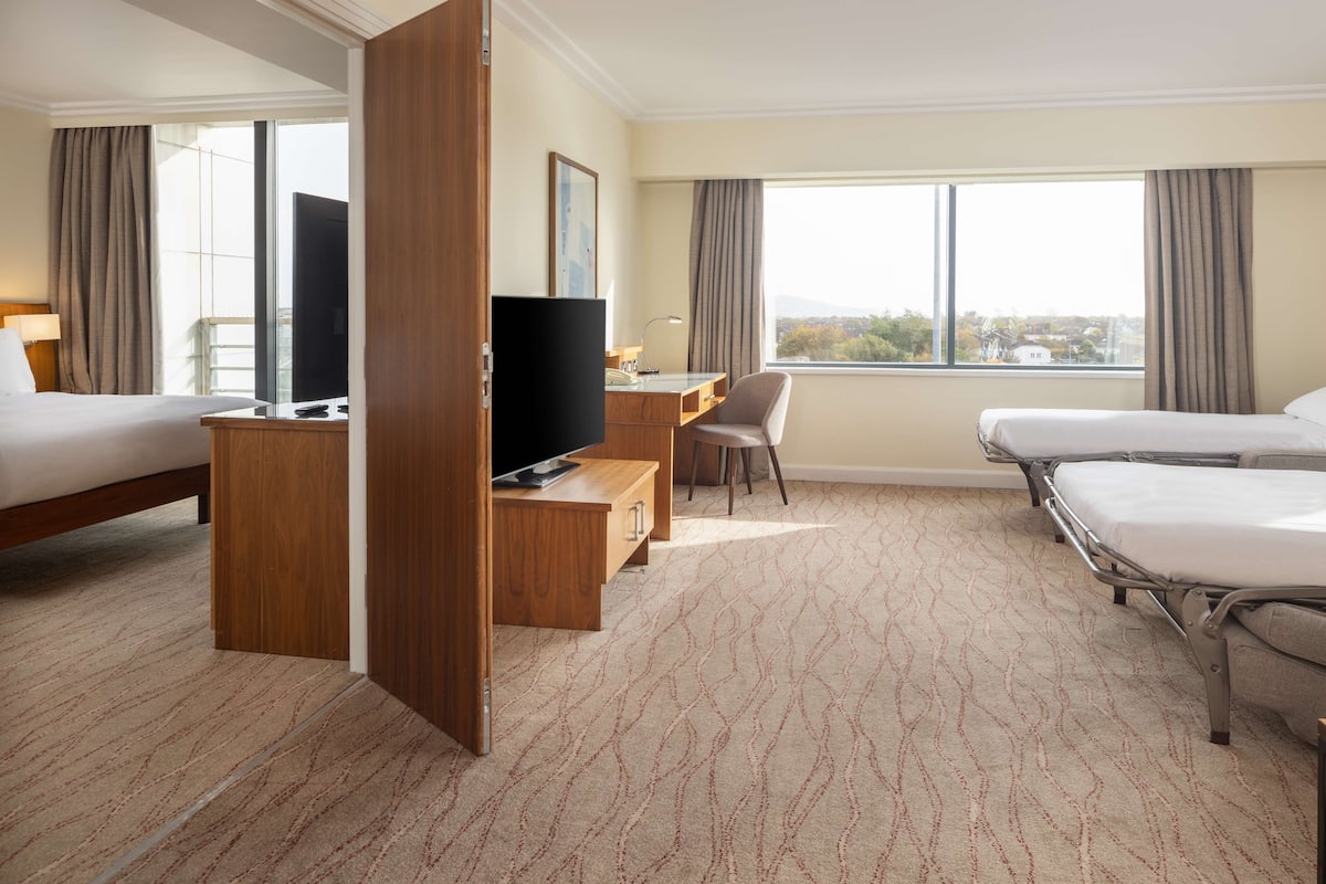 Une chambre d’hôtel avec deux lits, un bureau avec une télévision, une chaise et une grande fenêtre donnant sur un beau paysage.