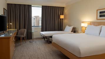 A hotel room with a bed, a desk, a chair, a small table, and a TV.