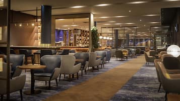 A modern hotel lobby with a bar area, seating arrangements, and a large plant.