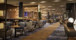Un hall d’hôtel moderne doté d’un bar, de différents espaces de détente et d’une grande plante.