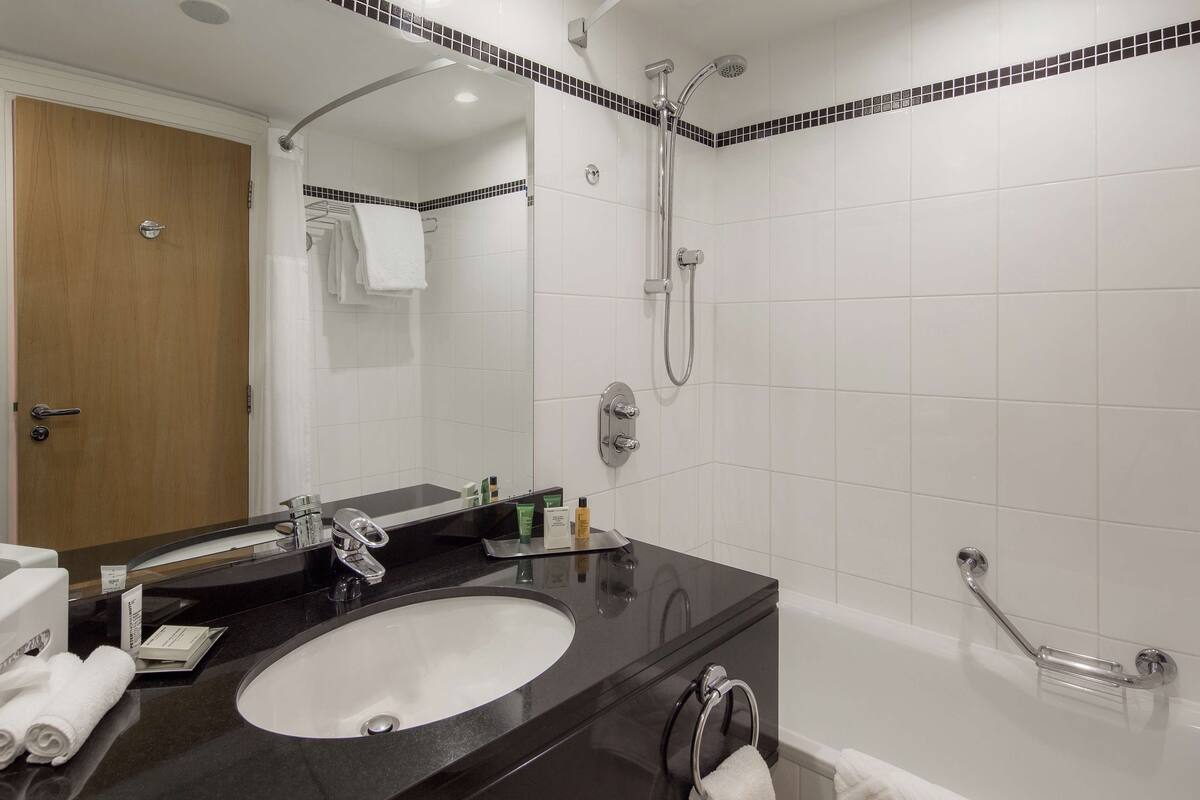 Une salle de bain avec un lavabo sur un plan de toilette noir, un miroir, une douche avec un pommeau de douche amovible et un porte-serviettes.