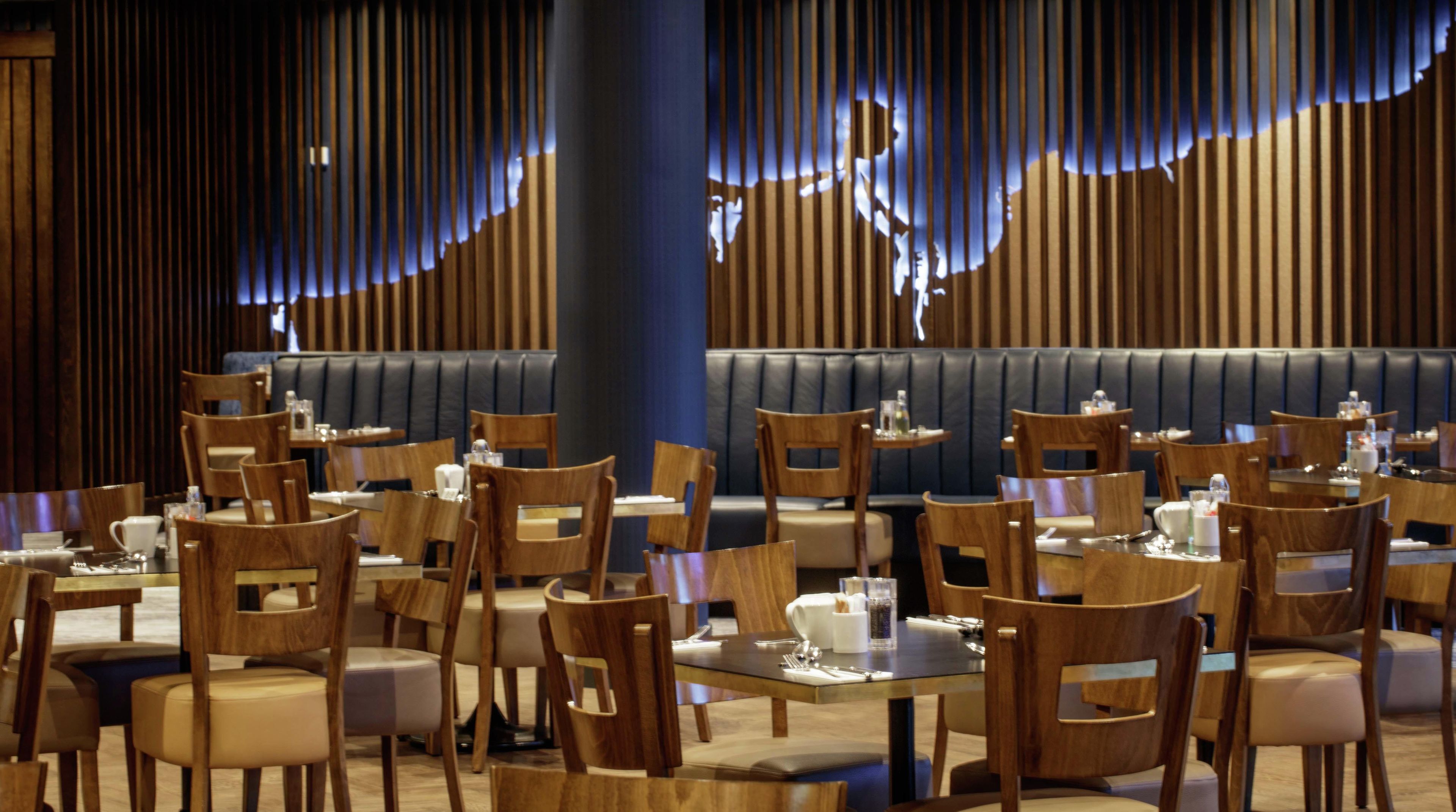L’intérieur d’un restaurant avec des banquettes et des tables, des chaises en bois et un mur éclairé en bleu.