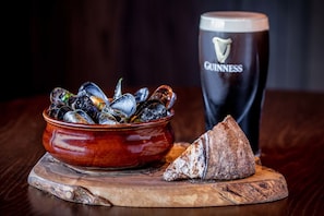 Un bol de moules, un verre de bière Guinness et une tranche de pain sur une planche en bois.