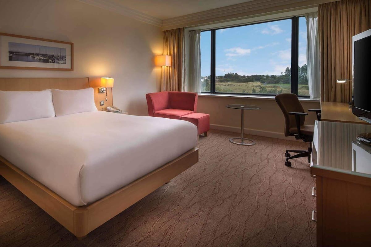 Une chambre d’hôtel avec un grand lit, un bureau avec une chaise, une petite table et un téléviseur.