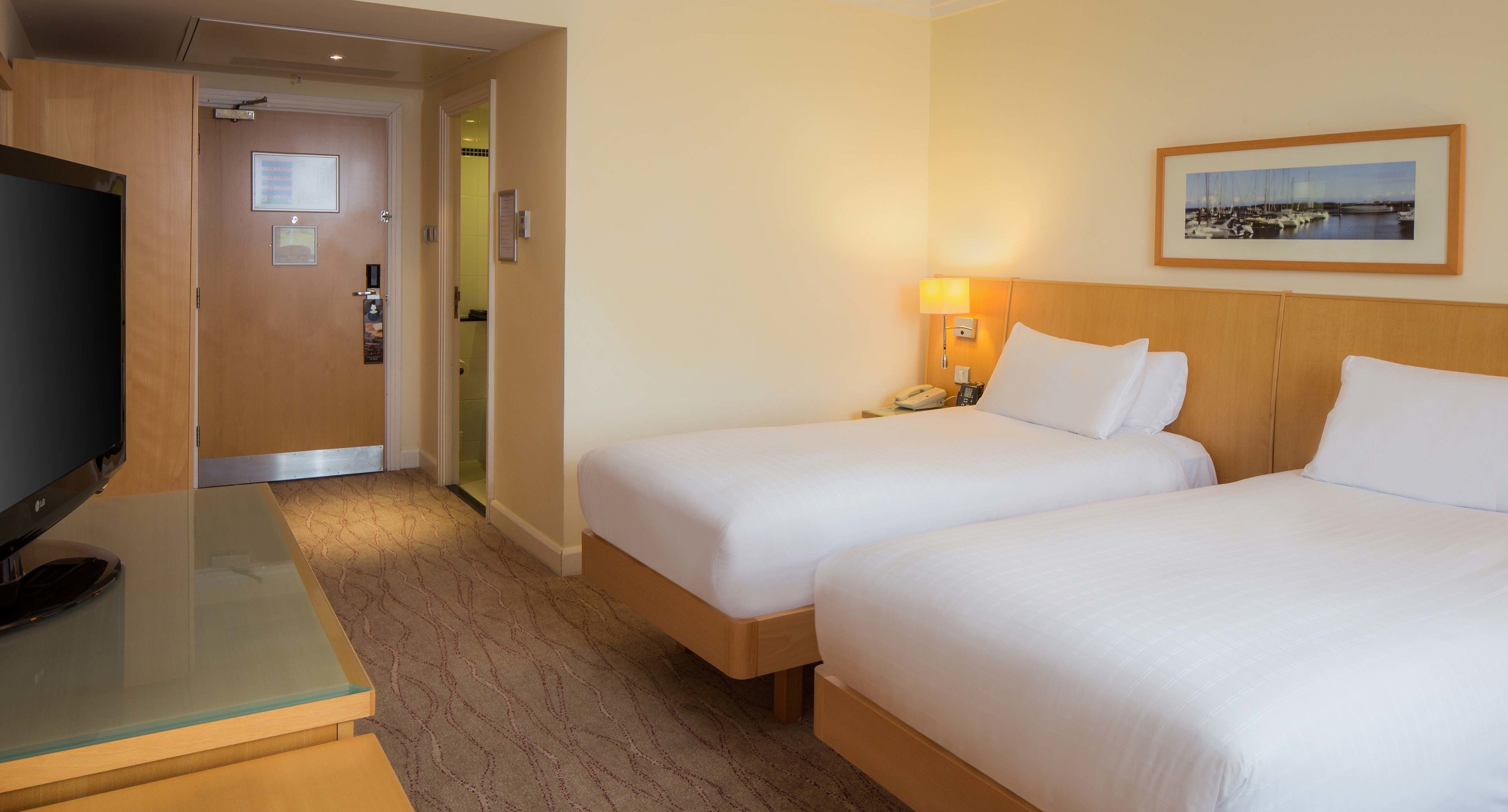 A hotel room with two beds, a TV, a desk, and a framed picture on the wall.