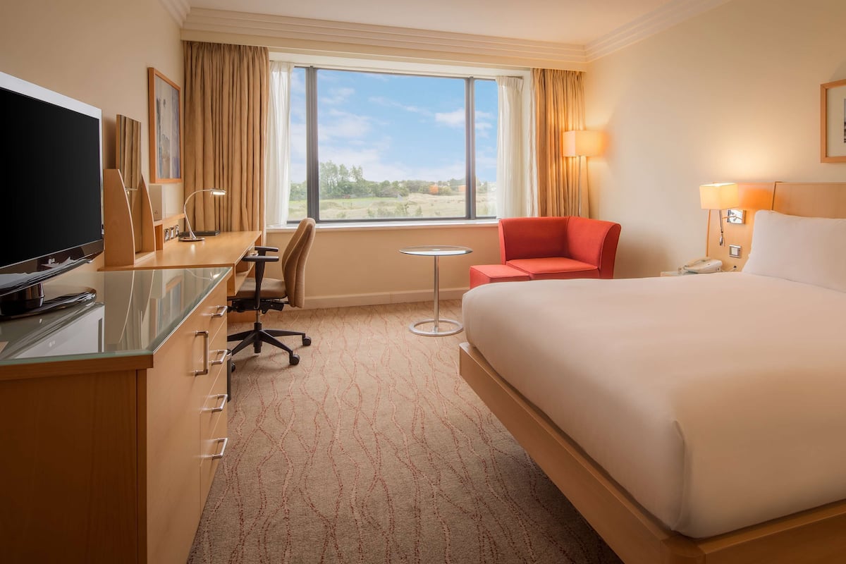 Une chambre d’hôtel avec un grand lit, un bureau avec une télévision, une chaise, une petite table et une fenêtre avec des rideaux.