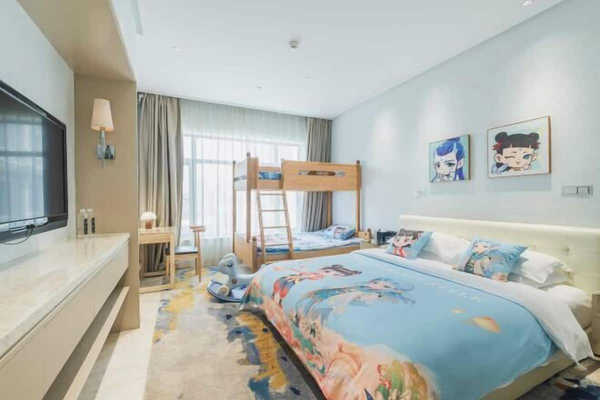 Habitación de hotel con literas, un escritorio con silla, televisor y un ventanal con cortinas.