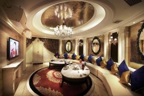 A luxurious room with a round coffee table, a sofa with cushions, a television, and a chandelier.
