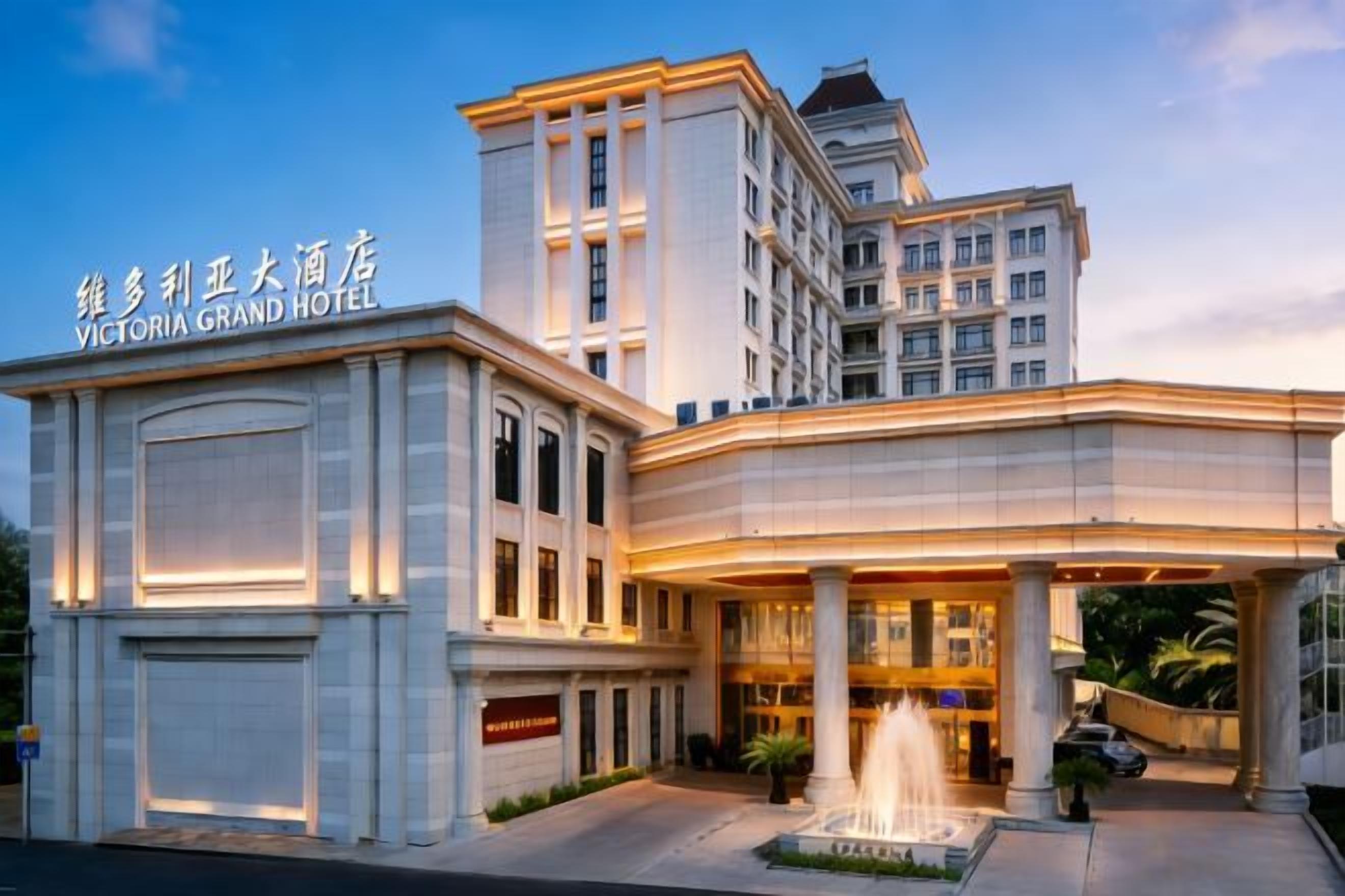 A grand hotel with a prominent entrance, a fountain, and a well-lit facade.