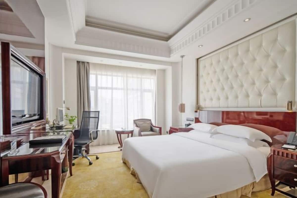 Una habitación de hotel con una cama grande, un escritorio con computadora, un televisor y una ventana con cortinas.