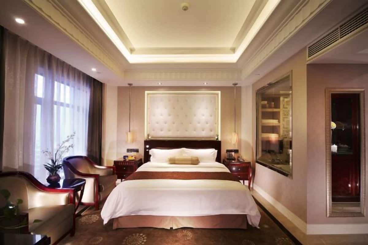 Habitación de hotel con una cama grande, dos mesitas de noche, una butaca, una planta en maceta y un espejo amplio.
