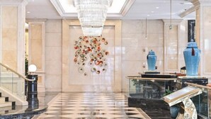 A lobby with a chandelier, a wall art installation, and a blue vase. - Victoria Grand Hotel (Wenzhou)