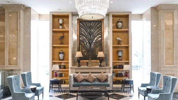 A lobby with a chandelier, a sofa with decorative pillows, and a coffee table. There are two side tables with lamps, and a large decorative wall piece. - Victoria Grand Hotel (Wenzhou)