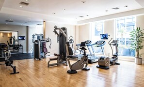Un gimnasio moderno con máquinas de cardio, equipo de entrenamiento con pesas y un amplio ventanal que proporciona luz natural.