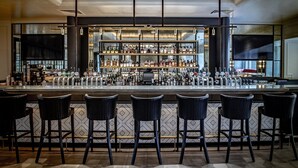 Una zona de bar con varios taburetes, una barra y estantes llenos de botellas.