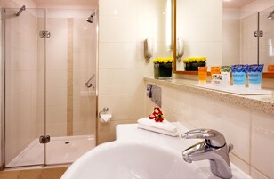 A modern bathroom with a glass-enclosed shower, a white sink with a chrome faucet, and a vanity with toiletries.