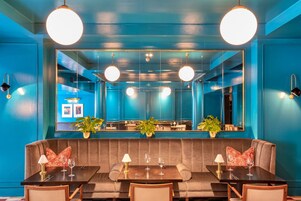 A restaurant with a blue interior, round ceiling lights, and a mirrored wall reflecting the dining area.