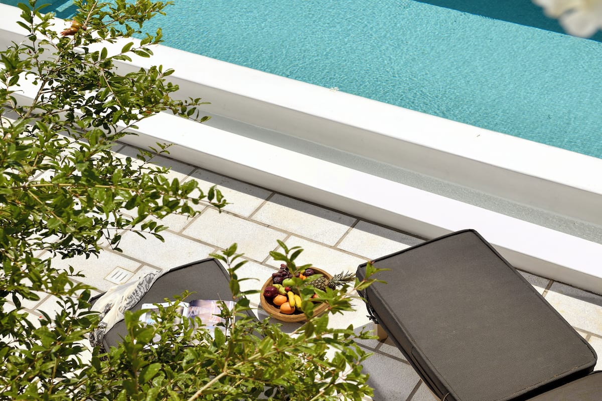 Un espace aménagé au bord de la piscine, avec une piscine blanche, des chaises longues et un panier de fruits.