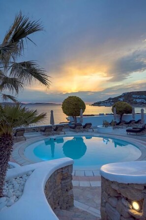 Zona de piscina con sillones y vista al mar al atardecer.