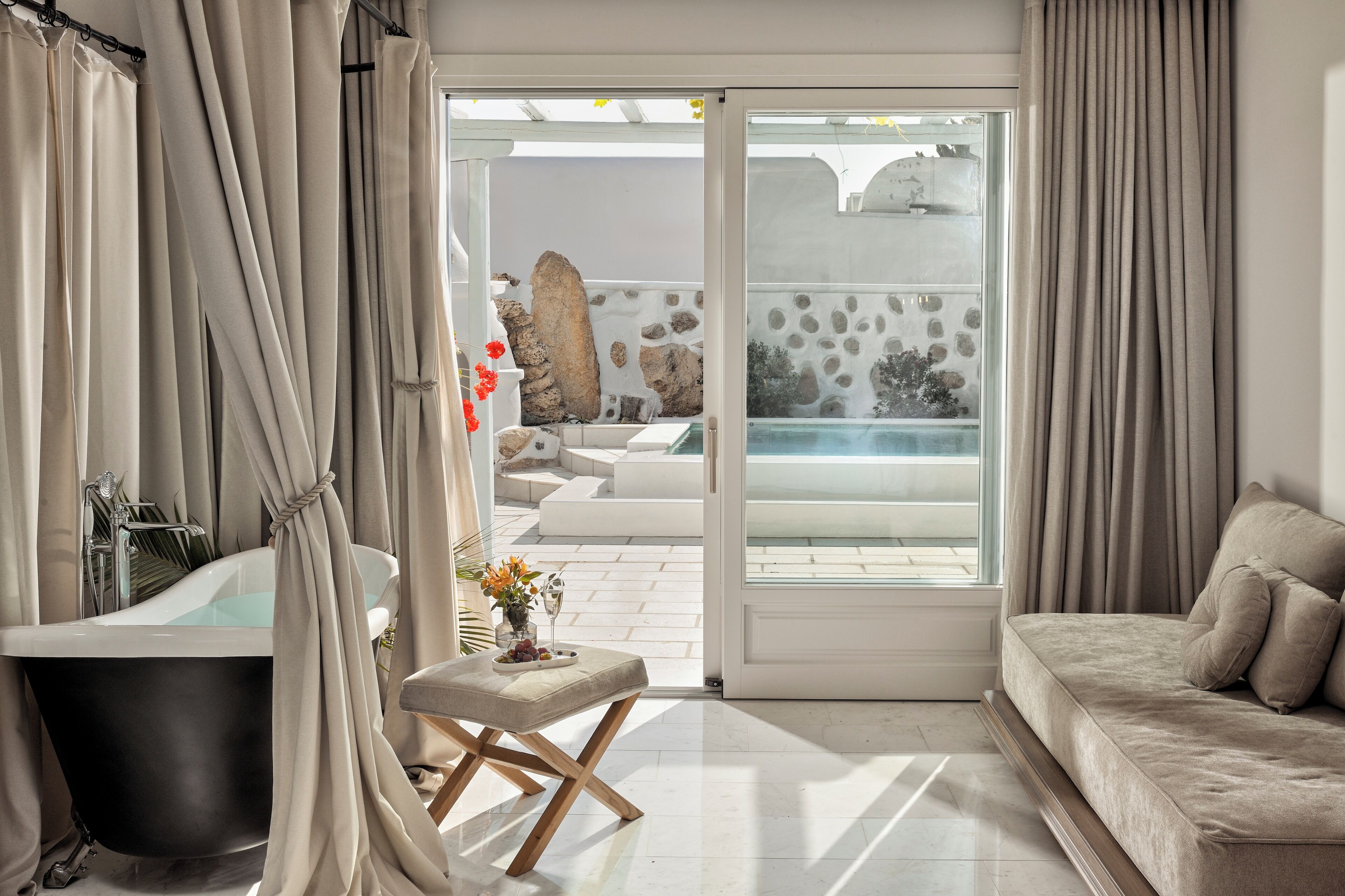 Un baño moderno con bañera, zona de ducha con mampara de vidrio y rincón de estar con vista a una piscina.