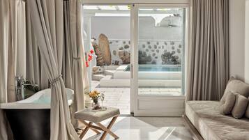 Un baño moderno con bañera, zona de ducha con mampara de vidrio y rincón de estar con vista a una piscina.