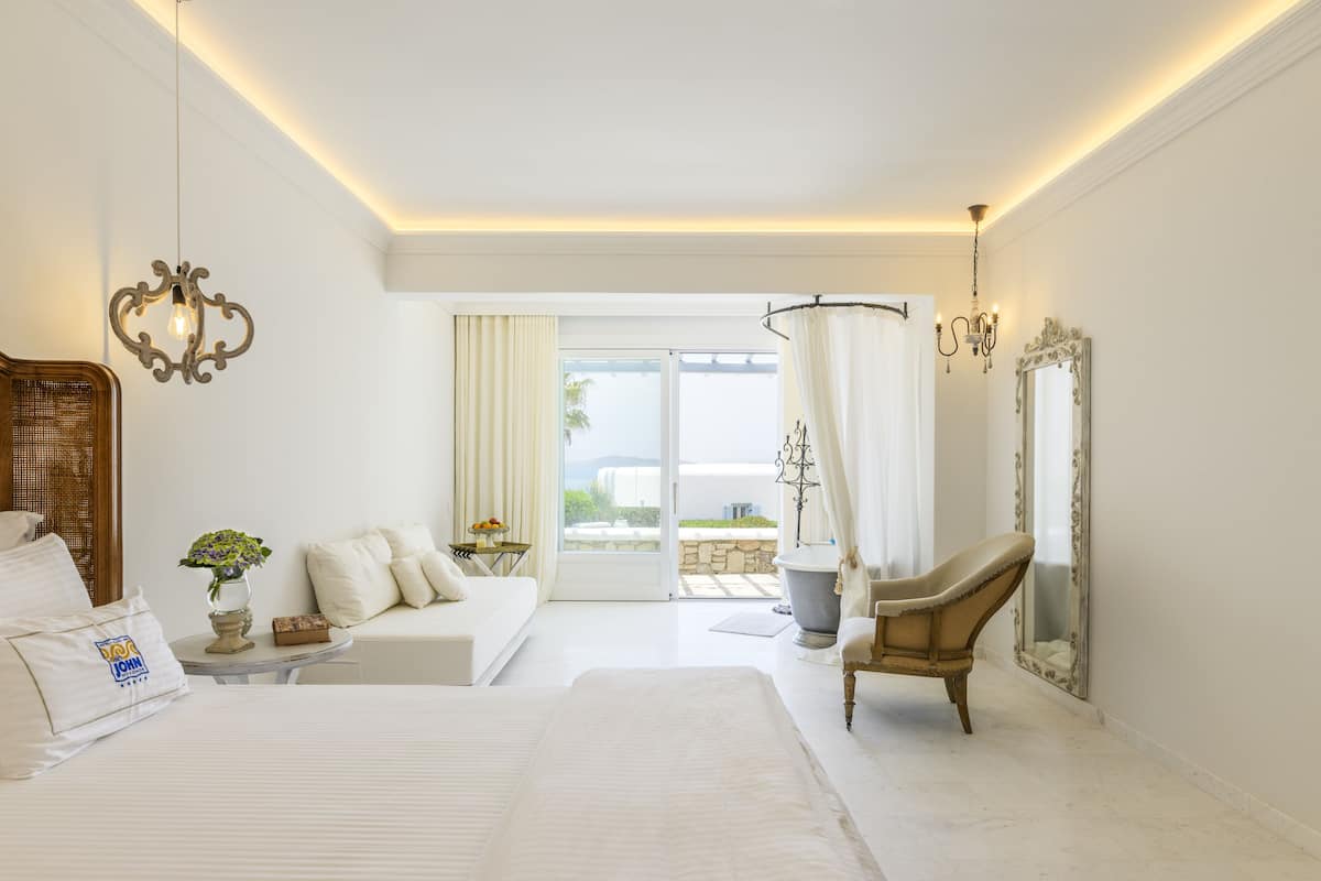 Une chambre spacieuse avec un grand lit, un coin salon avec un canapé et un fauteuil, ainsi qu’une baignoire.