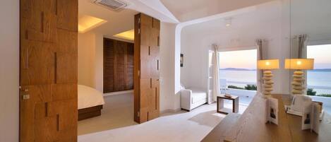 Une chambre d’hôtel moderne dotée d’un grand lit, d’une armoire en bois, d’un coin salon et offrant une vue sur la mer.