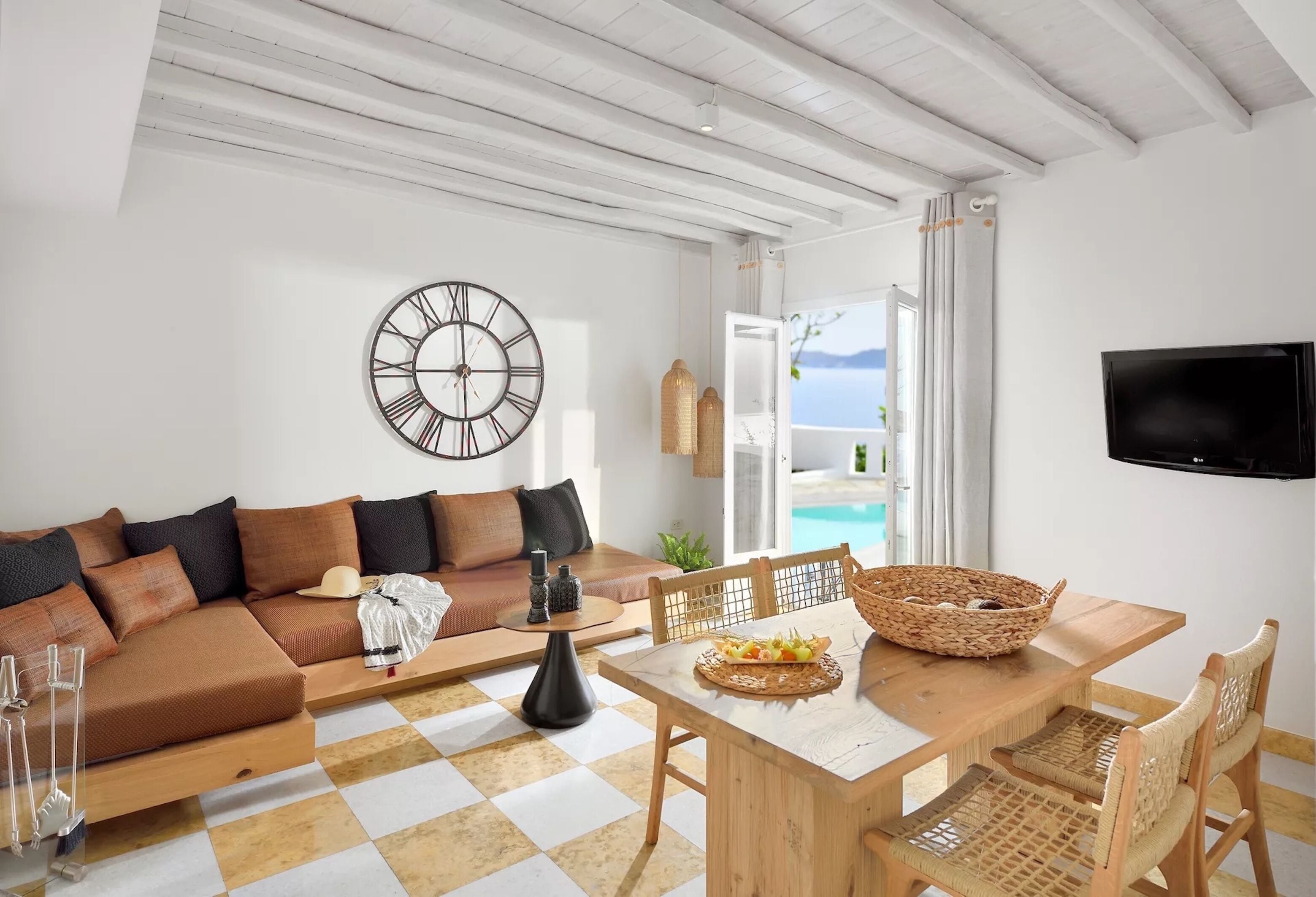 En moderne stue med sofa, spisebord og stole. Et stort vægur og et fladskærms-tv er synlige.