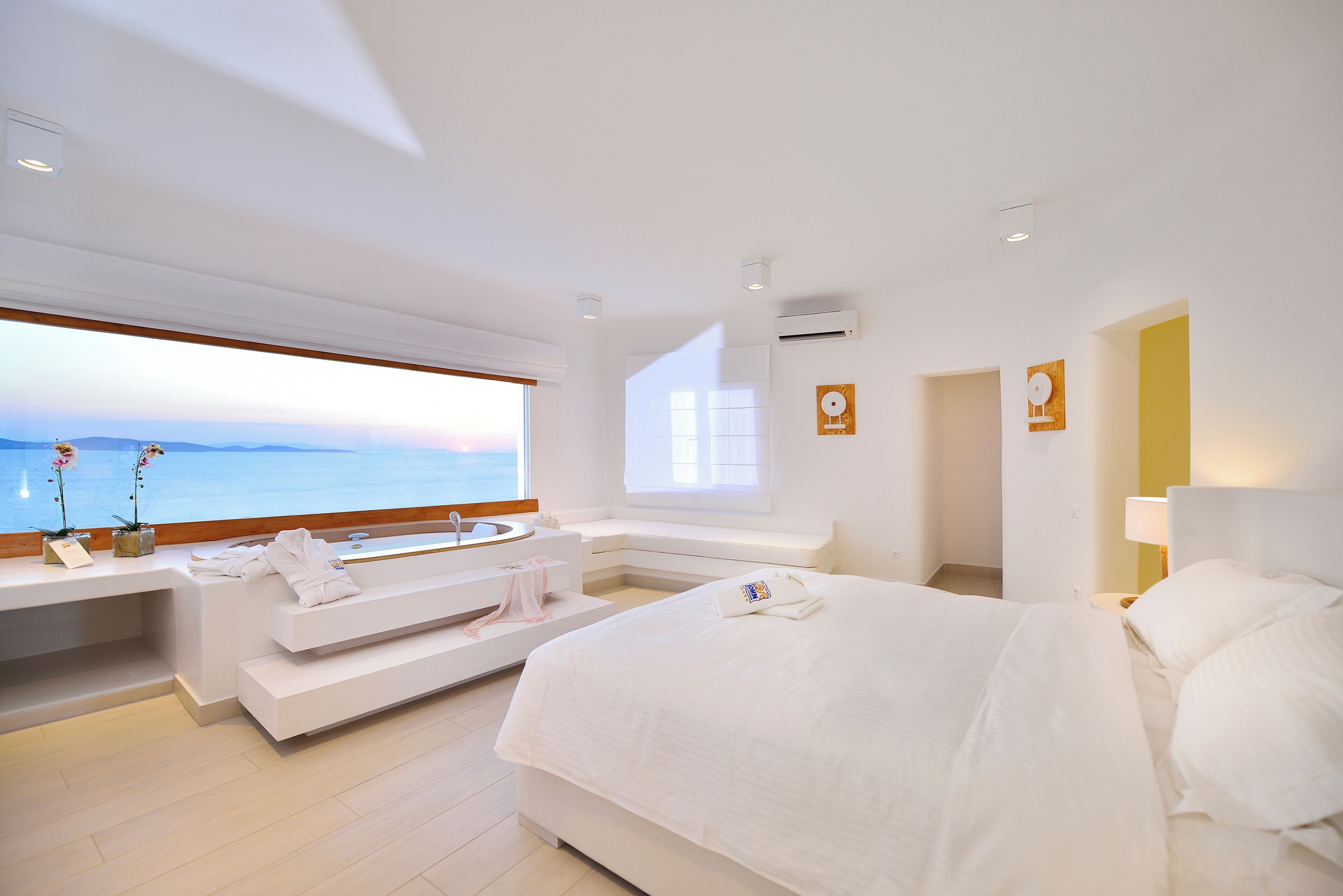 A modern hotel room with a large bed, a built-in bench with a sink, and a view of the sea.
