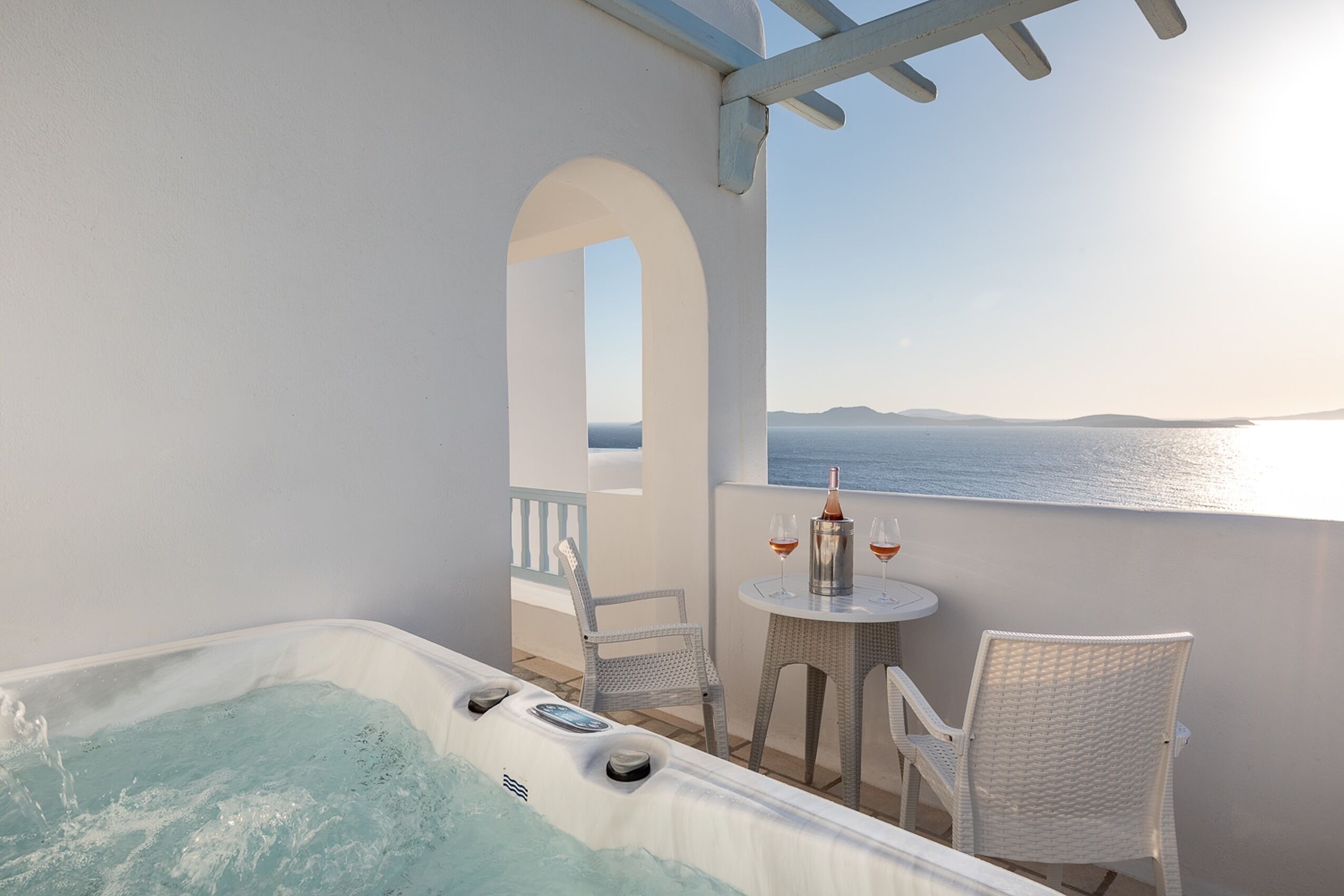 A balcony with a hot tub, two wicker chairs, and a table with a bottle and glasses.