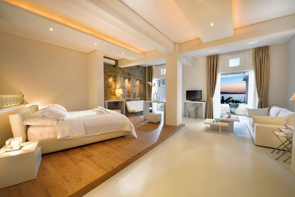 Une chambre d’hôtel moderne avec un plancher en bois, un lit, un coin salon avec un téléviseur et une vue sur la mer.