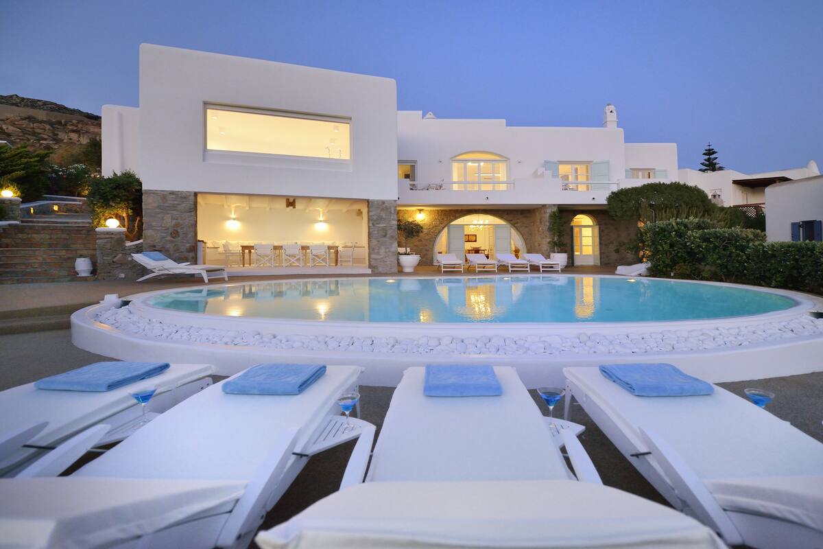 Une villa moderne dotée d’une piscine, de chaises longues et d’un espace extérieur bien éclairé.