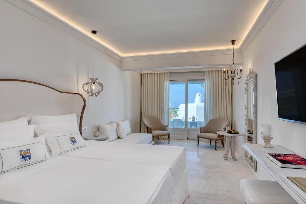 Une chambre d’hôtel avec un grand lit, deux fauteuils, une petite table, un téléviseur et un balcon avec vue.