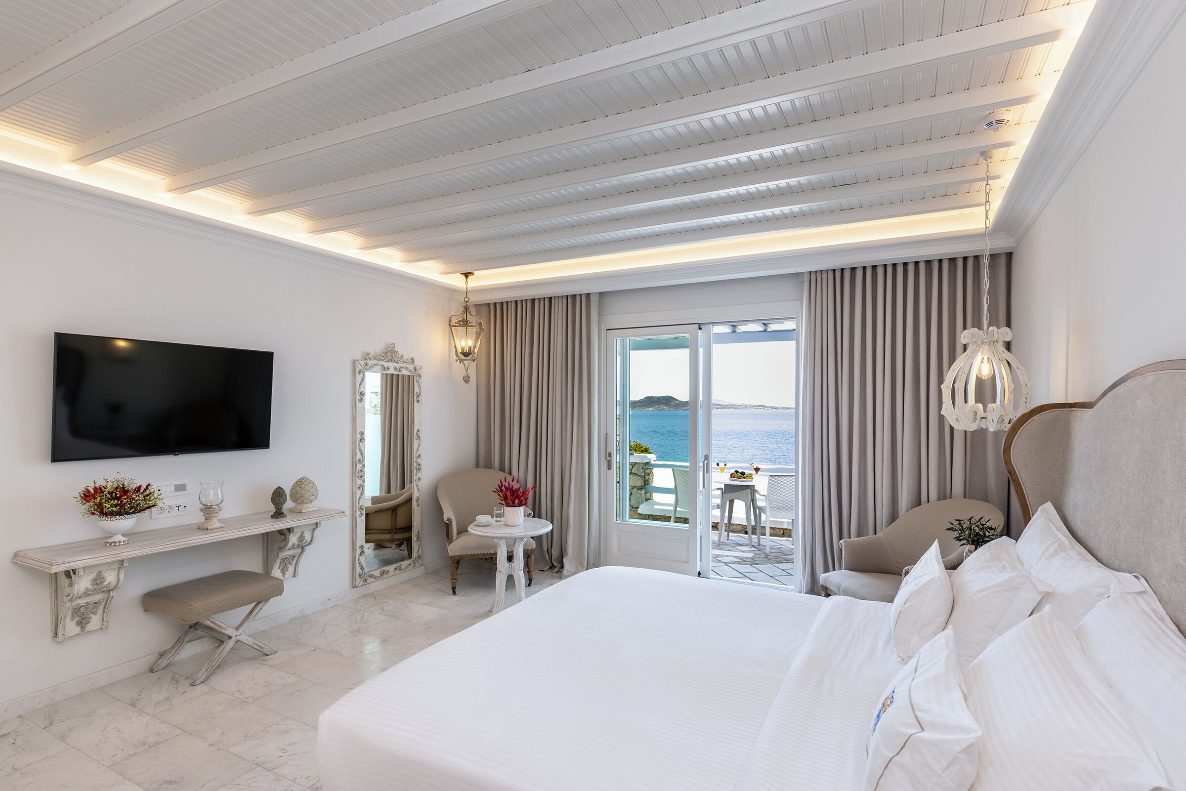 Habitación de hotel con una cama grande, televisión, escritorio con silla y balcón con vista al mar.