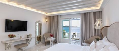 Habitación de hotel con una cama grande, televisión, escritorio con silla y balcón con vista al mar.