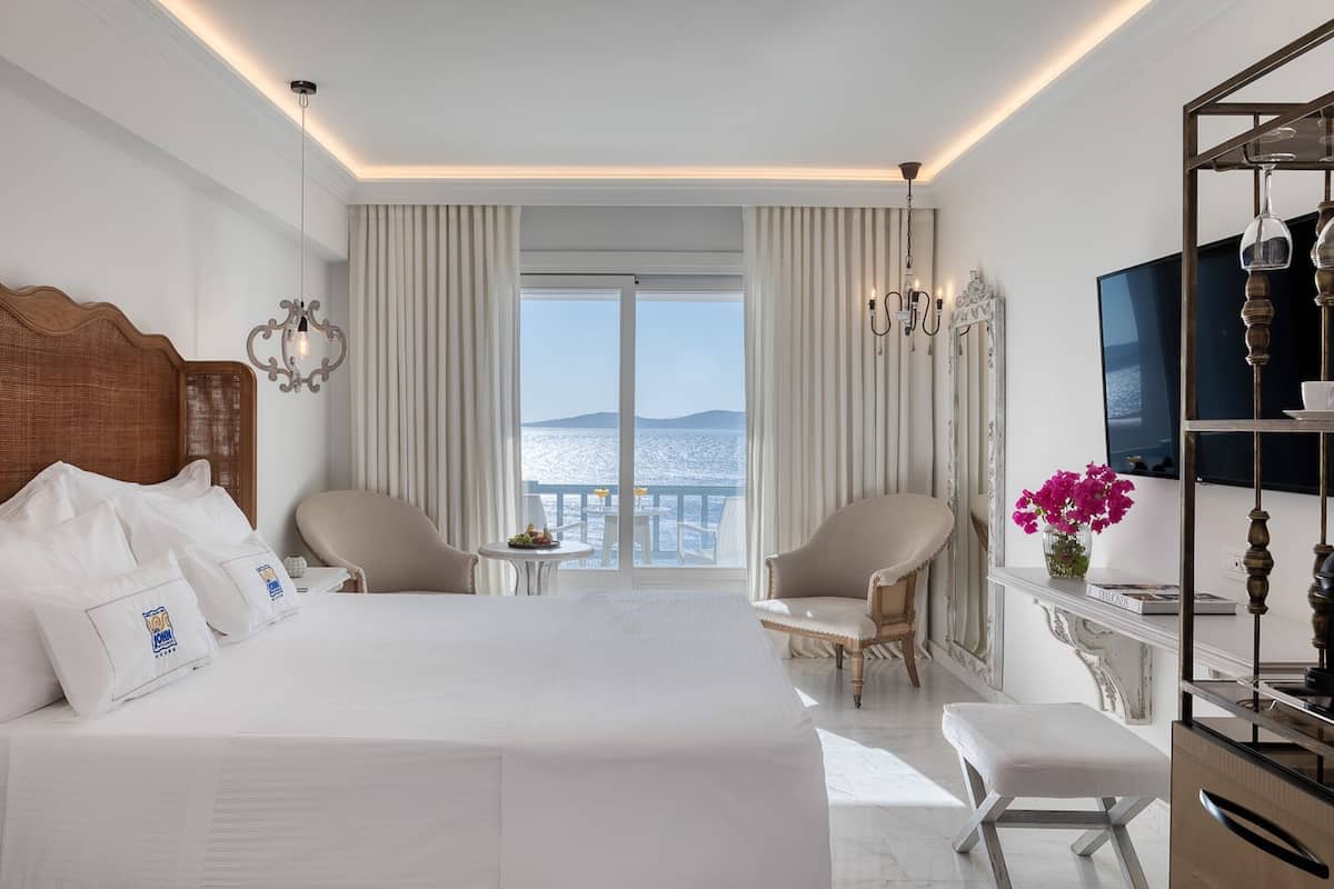 Une chambre d’hôtel avec un grand lit, deux fauteuils, une petite table, un téléviseur et une vue sur la mer.