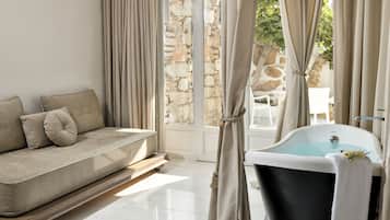 A modern bathroom with a bathtub, a sofa with cushions, and a stone wall.