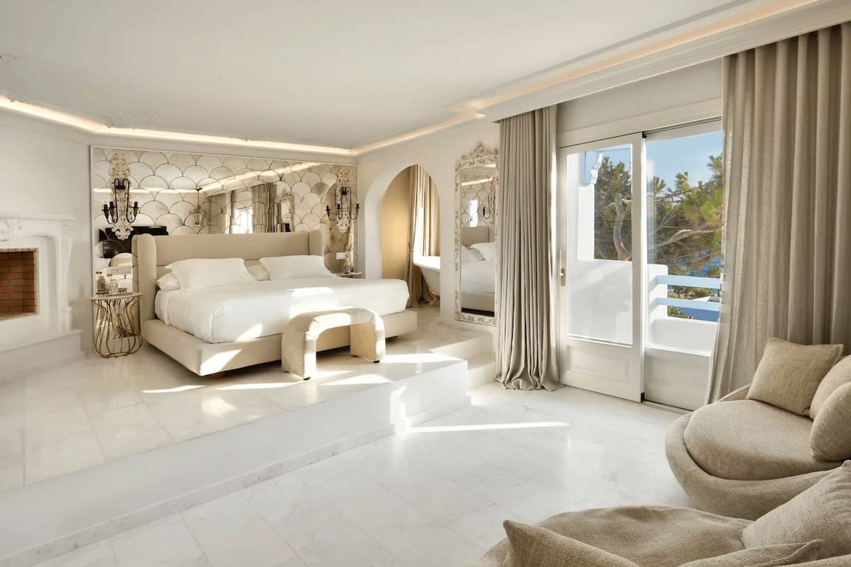 Une chambre spacieuse avec un grand lit, un coin salon avec un canapé et une vue sur l’extérieur grâce à de grandes fenêtres.