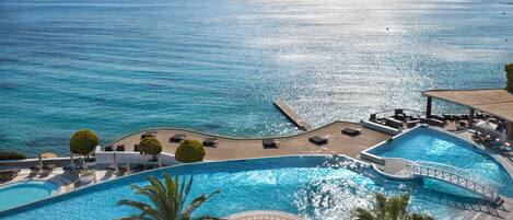 Una piscina de resort con vista al mar, palmeras y un puente.