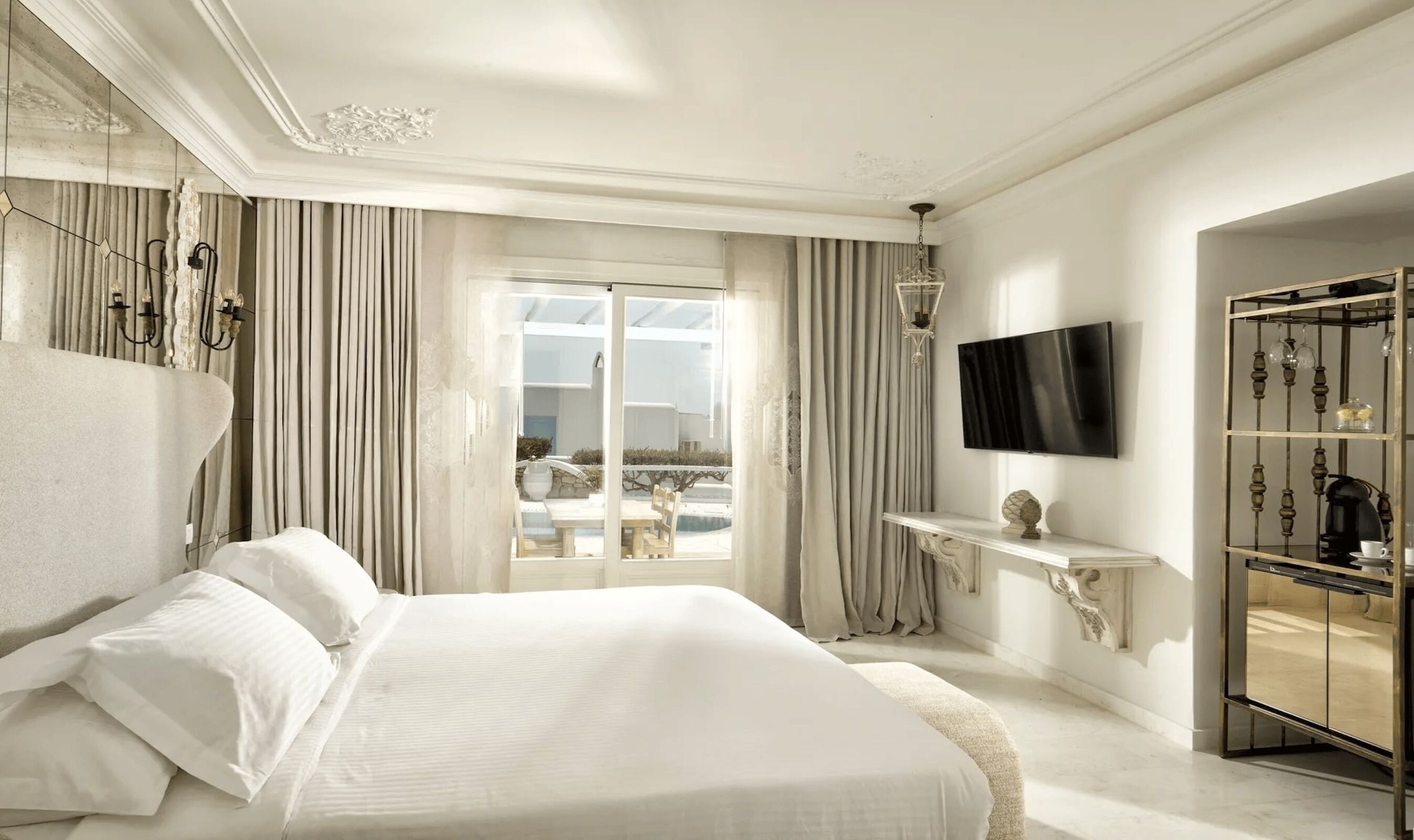Un dormitorio espacioso con una cama grande, televisión, una mesita de consola y vistas por la ventana.